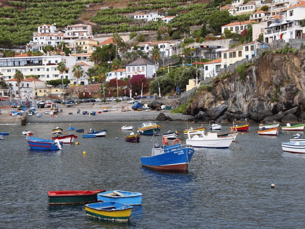 Ein Hafen mit bunten Fischerbooten. Im Hintergrund sind weisse Steildach-Häuser zu sehen, da am steilen Hang gebaut sind.